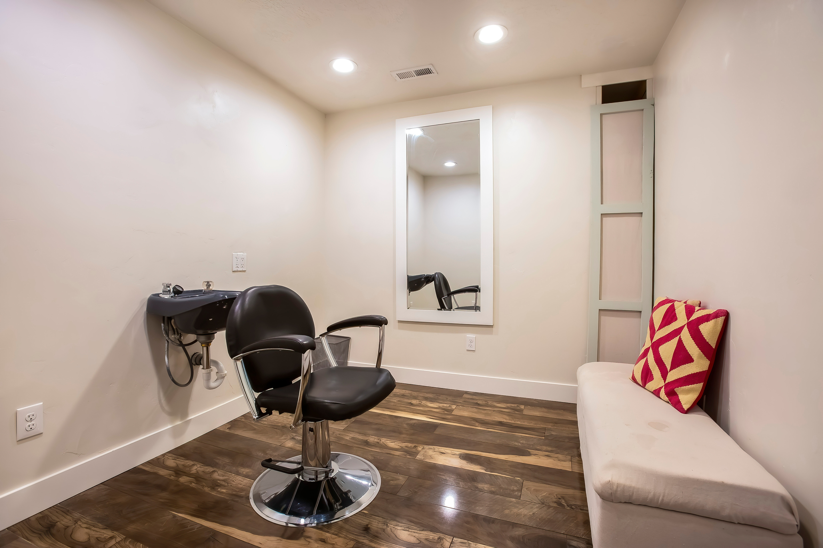 Hairdresser chair and backwash shampoo bowl inside salon with bench and mirror